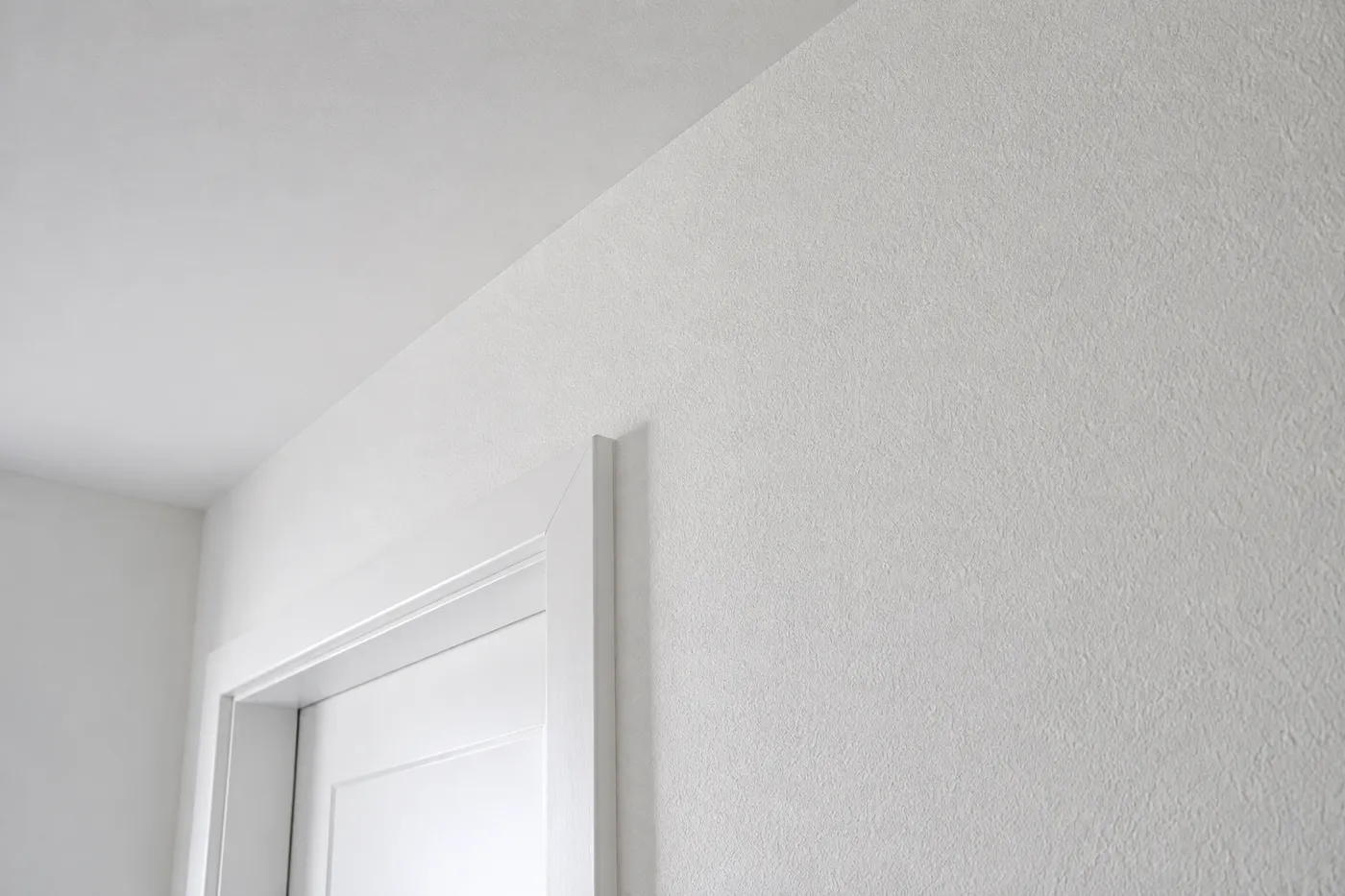 Weiss verputzte Wand mit feiner Struktur und heller Türlaibung